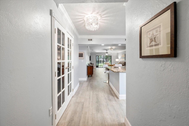 hallway with a textured wall, baseboards, ornamental molding, french doors, and light wood finished floors