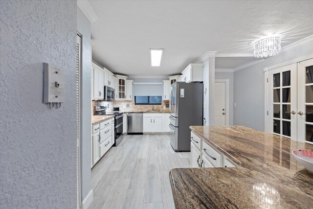 kitchen with stainless steel appliances, white cabinetry, backsplash, and stone countertops