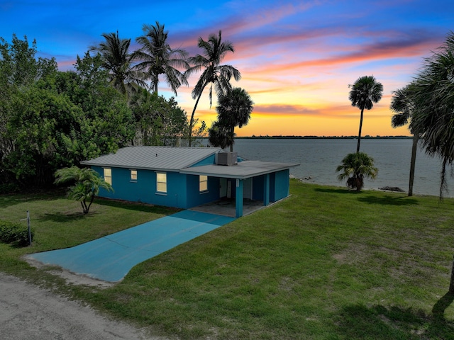 view of front of home with central air condition unit, a water view, a carport, and a lawn