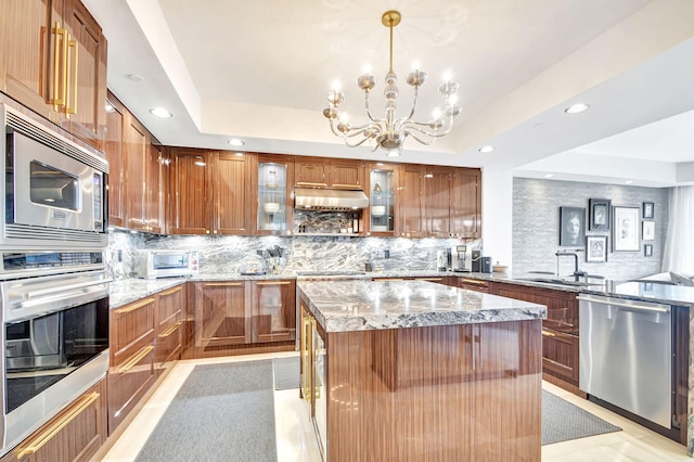 kitchen featuring light stone countertops, stainless steel appliances, a notable chandelier, backsplash, and a kitchen island