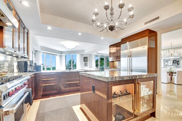 kitchen with premium appliances, a raised ceiling, decorative backsplash, and an inviting chandelier