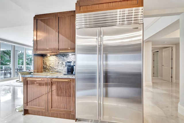 kitchen with backsplash, floor to ceiling windows, light stone countertops, and stainless steel built in fridge