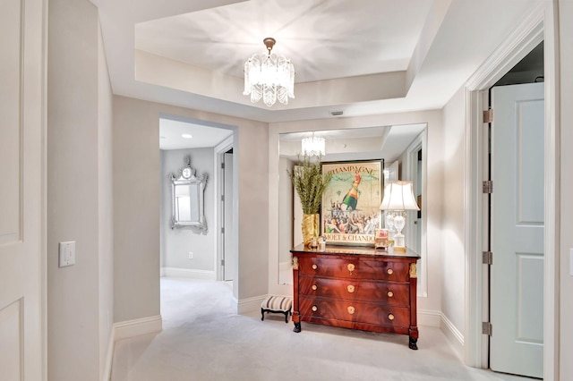 hallway with a tray ceiling, light carpet, and a chandelier