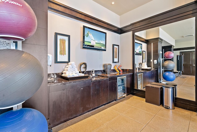 bar featuring dark brown cabinets, beverage cooler, and dark stone countertops