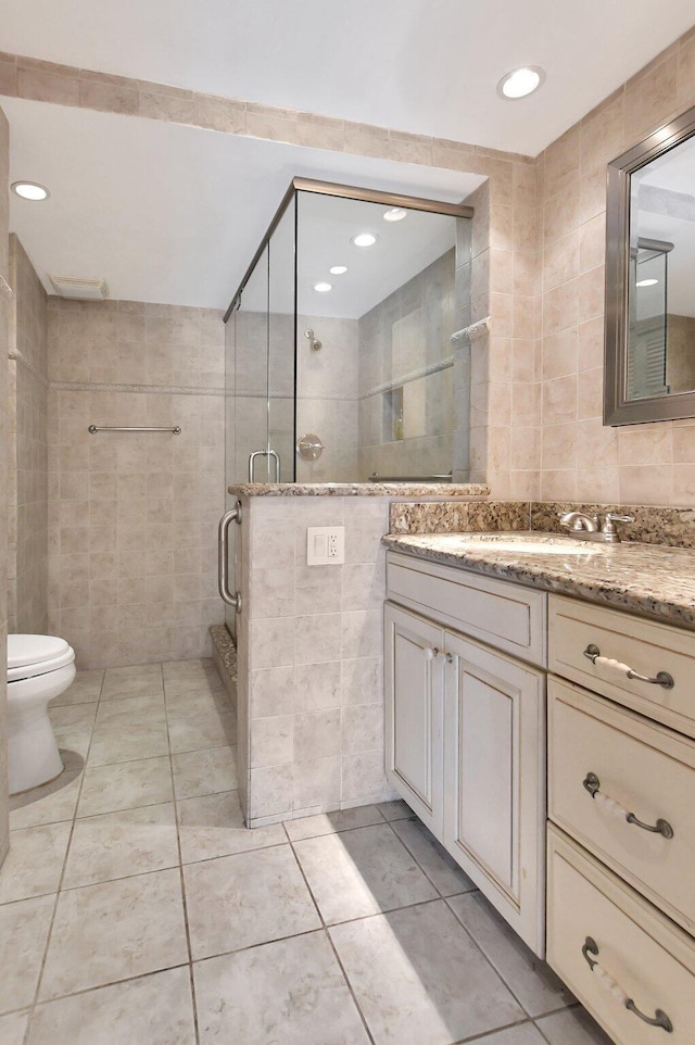 bathroom featuring tile patterned floors, toilet, a shower with shower door, tile walls, and vanity