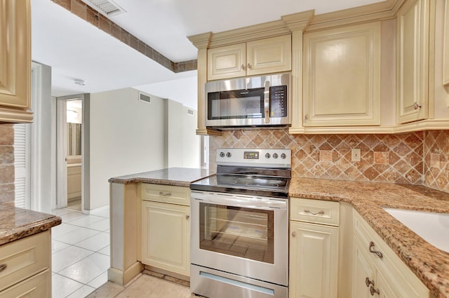 kitchen with backsplash, stainless steel appliances, light stone countertops, and cream cabinetry