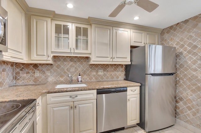 kitchen featuring appliances with stainless steel finishes, sink, backsplash, light stone counters, and cream cabinets