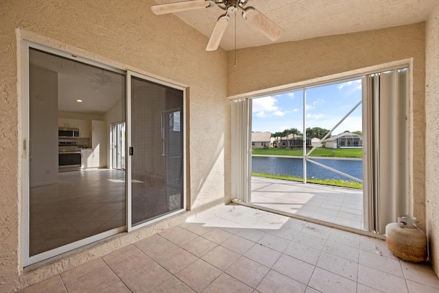 unfurnished sunroom featuring ceiling fan and a water view