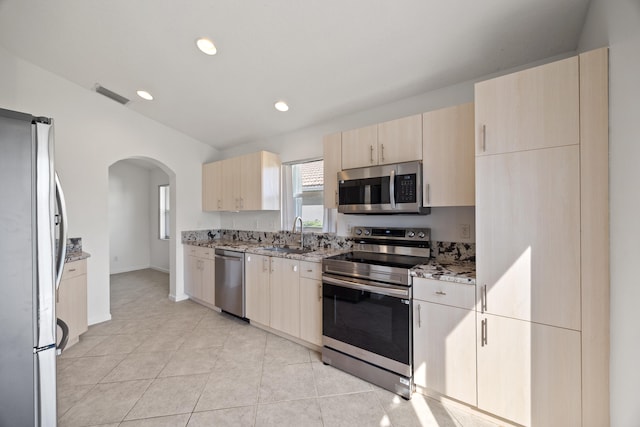 kitchen with light stone countertops, stainless steel appliances, sink, light brown cabinets, and light tile patterned floors