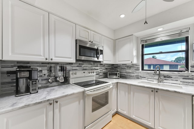 kitchen with light stone countertops, backsplash, white range with electric stovetop, sink, and white cabinetry