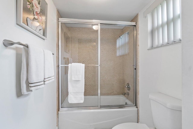 bathroom featuring combined bath / shower with glass door and toilet