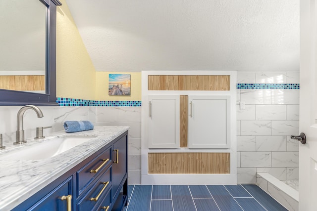 bathroom with a textured ceiling, lofted ceiling, vanity, tile walls, and a tile shower