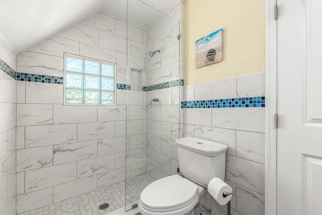 bathroom with toilet, a tile shower, vaulted ceiling, and tile walls