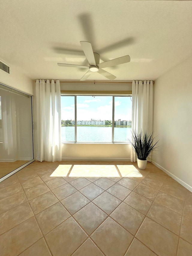 tiled spare room featuring a water view and ceiling fan