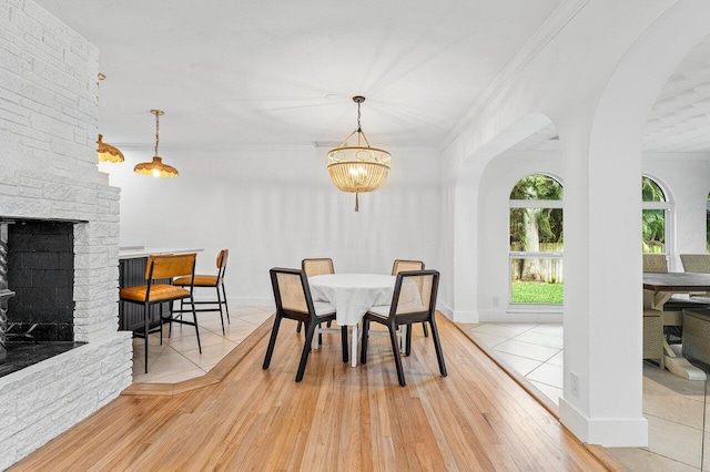 dining space with a brick fireplace, a notable chandelier, ornamental molding, and light hardwood / wood-style flooring