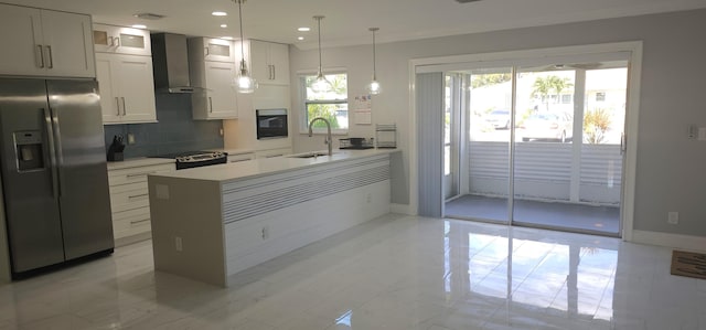 kitchen featuring sink, hanging light fixtures, wall chimney range hood, white cabinets, and appliances with stainless steel finishes