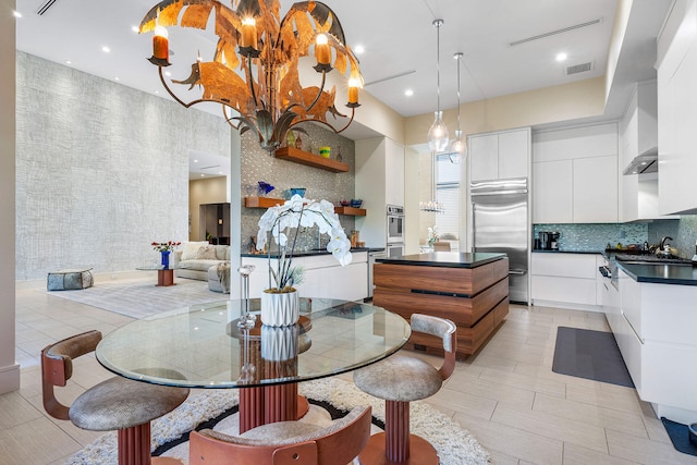 kitchen with appliances with stainless steel finishes, a kitchen island, light tile patterned floors, decorative light fixtures, and white cabinetry