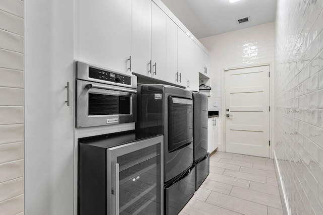 kitchen featuring oven, wine cooler, white cabinetry, and washing machine and clothes dryer