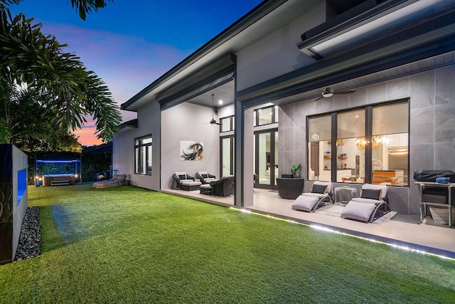 back house at dusk with a lawn, a patio, and ceiling fan