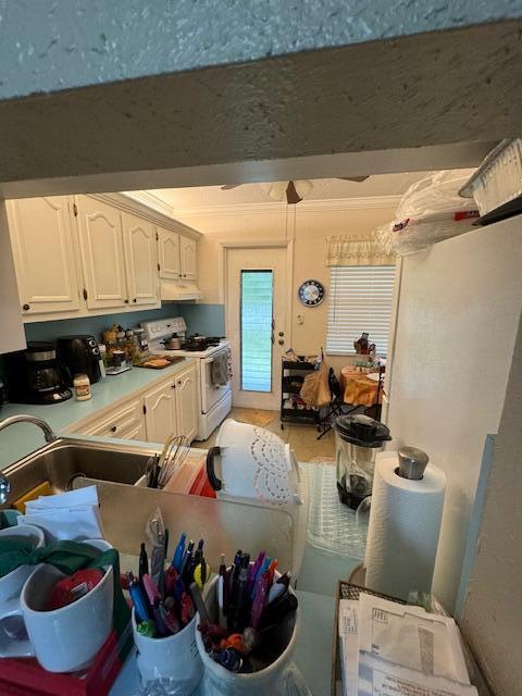 kitchen featuring white gas stove, sink, and white cabinets