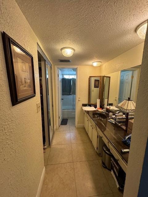 hallway with a textured ceiling and light tile floors