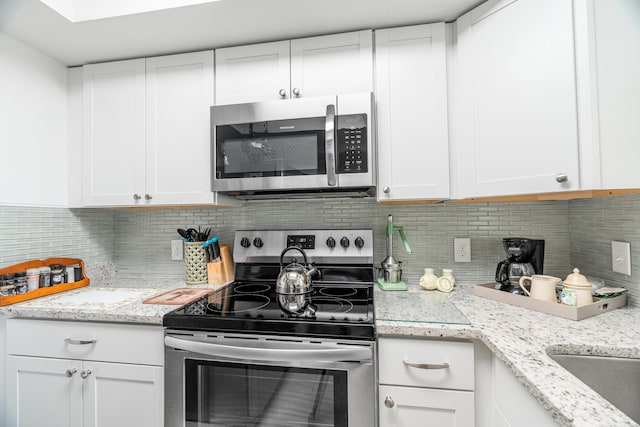 kitchen featuring white cabinets, light stone countertops, backsplash, and stainless steel appliances