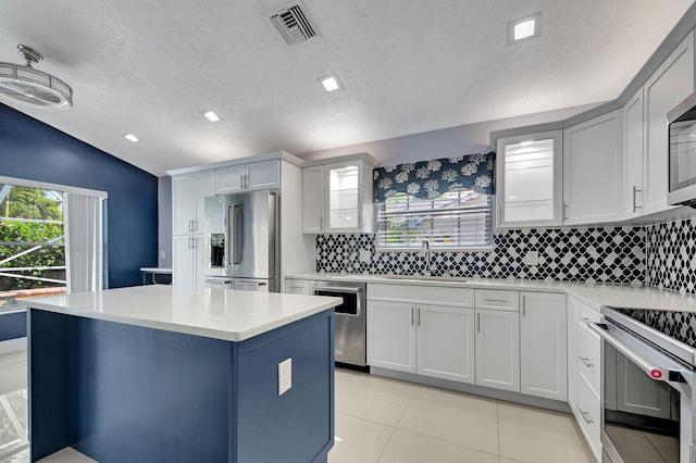 kitchen with light tile patterned floors, appliances with stainless steel finishes, decorative backsplash, vaulted ceiling, and sink