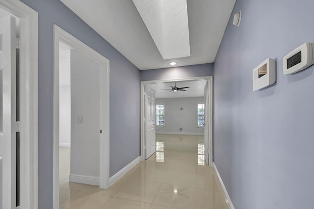 hall with light tile patterned flooring and a skylight