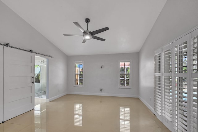 tiled spare room with plenty of natural light, a barn door, ceiling fan, and vaulted ceiling