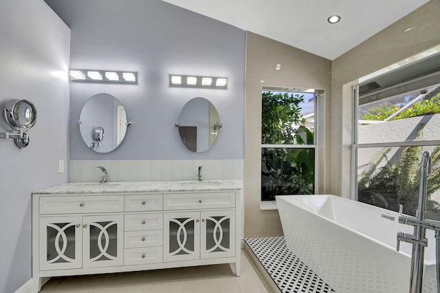 bathroom featuring a washtub, double sink vanity, vaulted ceiling, and tile patterned flooring