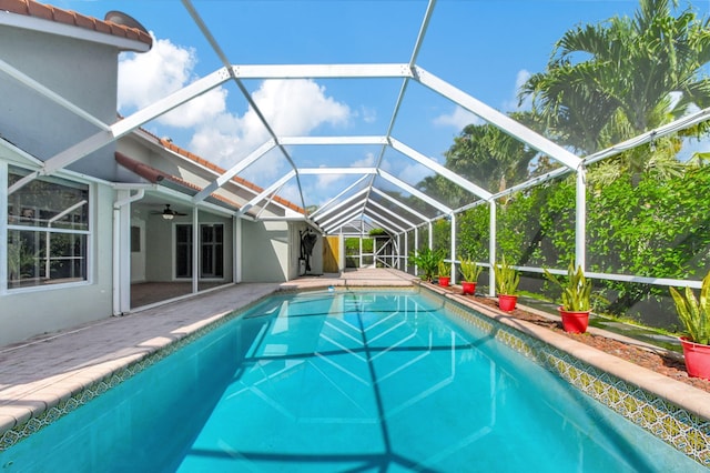 view of swimming pool featuring glass enclosure, a patio area, and ceiling fan