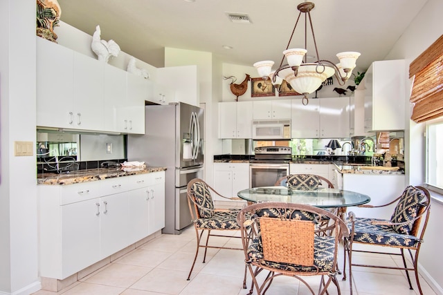 kitchen with appliances with stainless steel finishes, white cabinets, light tile floors, and hanging light fixtures