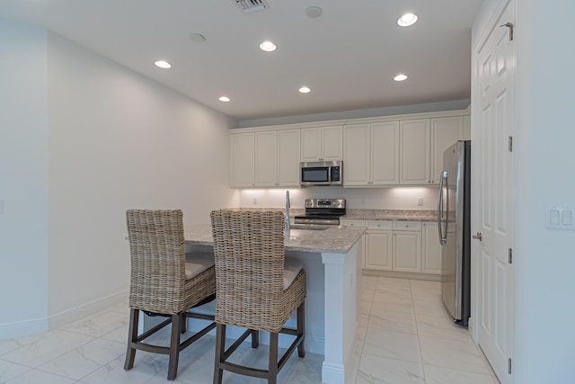 kitchen featuring a breakfast bar area, white cabinetry, light stone counters, a center island with sink, and appliances with stainless steel finishes