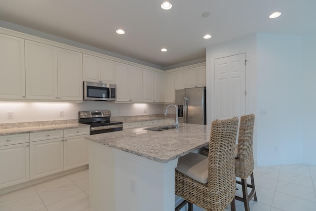 kitchen with appliances with stainless steel finishes, a breakfast bar, white cabinetry, an island with sink, and sink