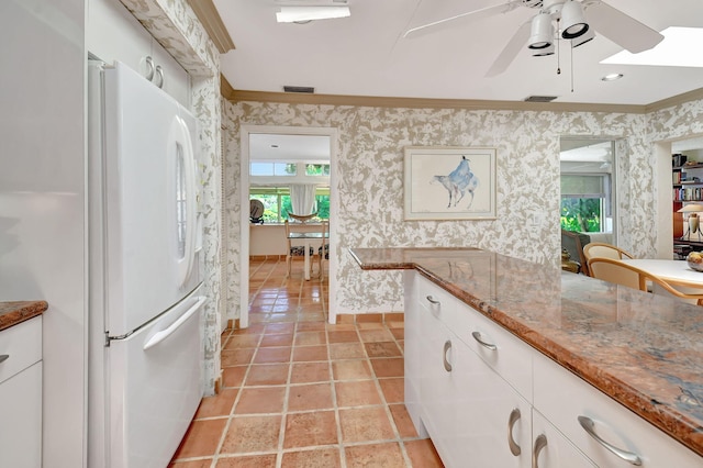 kitchen with light stone countertops, ornamental molding, ceiling fan, white refrigerator, and white cabinetry