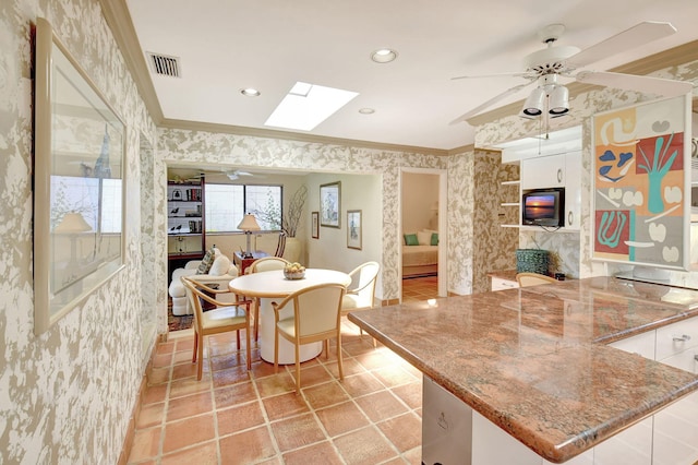 dining area with a fireplace, a skylight, ceiling fan, and crown molding