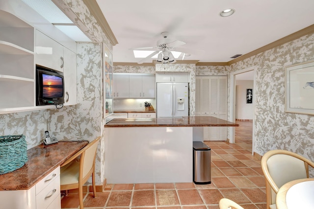 kitchen featuring white cabinets, crown molding, white fridge with ice dispenser, and kitchen peninsula