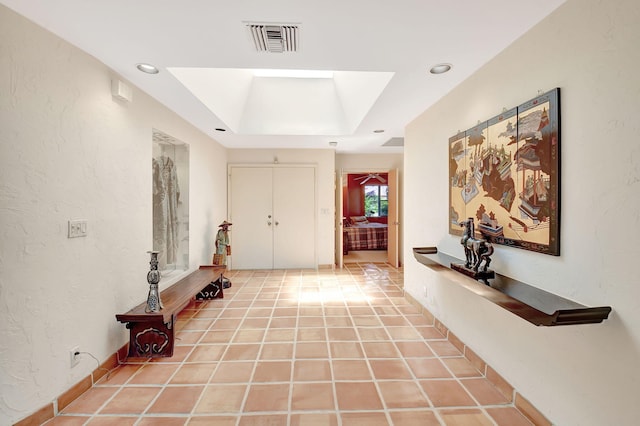 hall featuring a skylight, tile patterned floors, and a tray ceiling