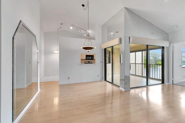 spare room featuring baseboards, track lighting, high vaulted ceiling, and light wood-style floors