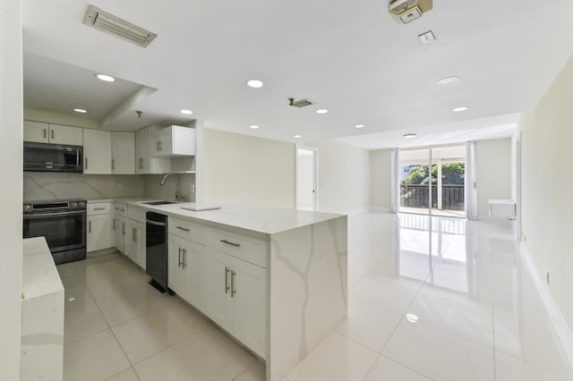 kitchen with black appliances, sink, white cabinetry, light stone counters, and kitchen peninsula