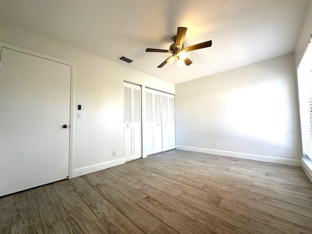 unfurnished bedroom with ceiling fan, two closets, and light wood-type flooring