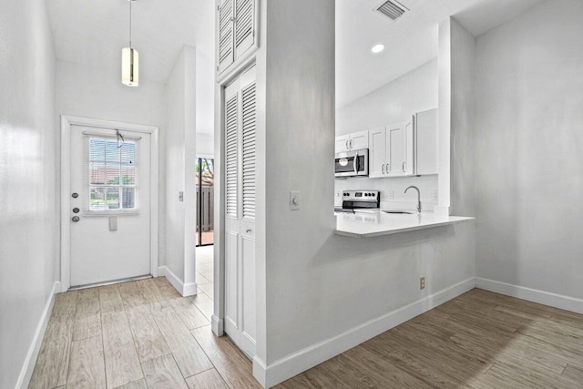 interior space with pendant lighting, white cabinets, sink, light wood-type flooring, and appliances with stainless steel finishes