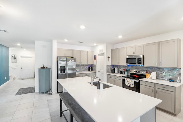 kitchen featuring sink, a kitchen bar, stainless steel appliances, backsplash, and a center island with sink