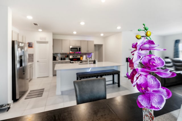 kitchen with a kitchen island with sink, tasteful backsplash, gray cabinetry, appliances with stainless steel finishes, and light tile patterned floors