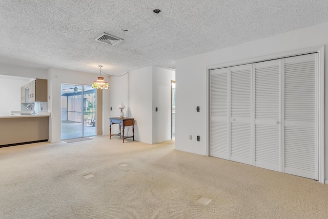 unfurnished living room with light carpet, a textured ceiling, and sink