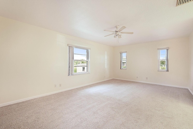 empty room with visible vents, light carpet, a wealth of natural light, and baseboards