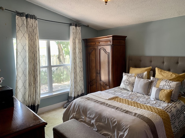 bedroom with lofted ceiling, light tile patterned floors, and a textured ceiling