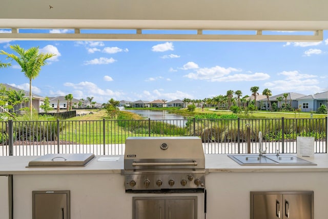 view of patio with a water view, fence, a grill, exterior kitchen, and a residential view