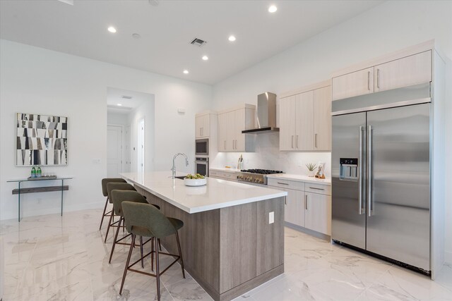 kitchen featuring decorative light fixtures, light brown cabinetry, wall chimney range hood, appliances with stainless steel finishes, and backsplash