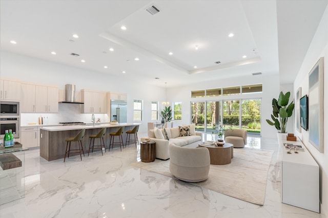 living area with a tray ceiling, marble finish floor, a high ceiling, and visible vents